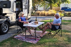 Couple enjoying wine and nibbles in the sun, next to their caravan.